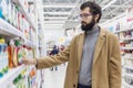 Young man in the supermarket in the household chemicals department. Large selection of products. A brunette with glasses and a bea Royalty Free Stock Photo